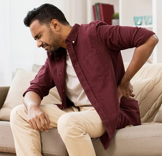 a man sitting on a couch, in pain and holding his hand behind his back